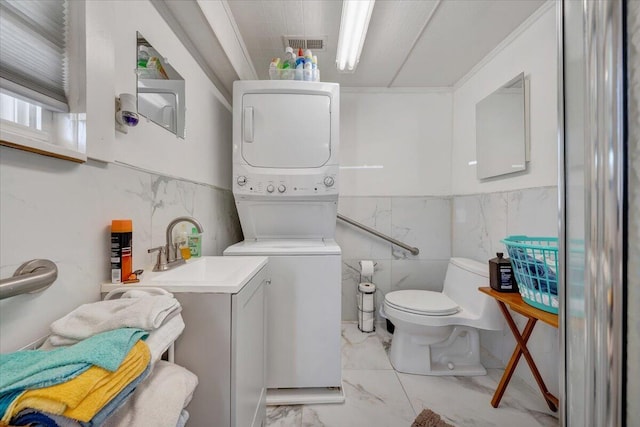 bathroom featuring tile walls, toilet, vanity, and stacked washer and clothes dryer