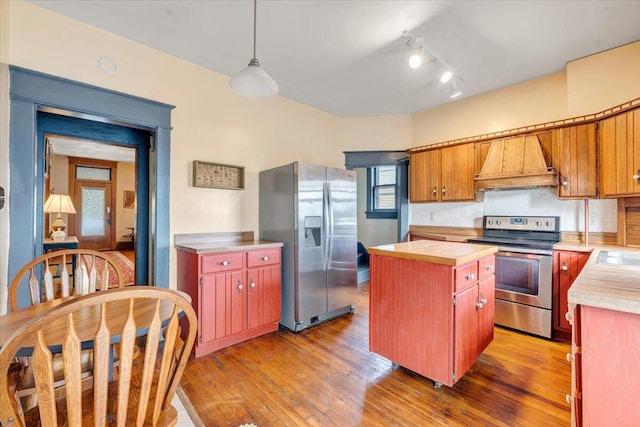 kitchen featuring wood-type flooring, a kitchen island, stainless steel appliances, decorative light fixtures, and premium range hood