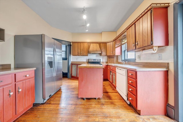 kitchen with sink, a center island, custom exhaust hood, appliances with stainless steel finishes, and light hardwood / wood-style floors