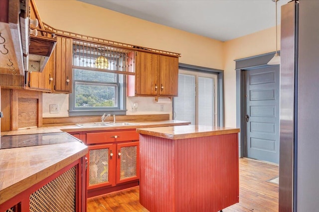 kitchen featuring sink, a kitchen island, decorative light fixtures, stainless steel refrigerator, and light hardwood / wood-style flooring