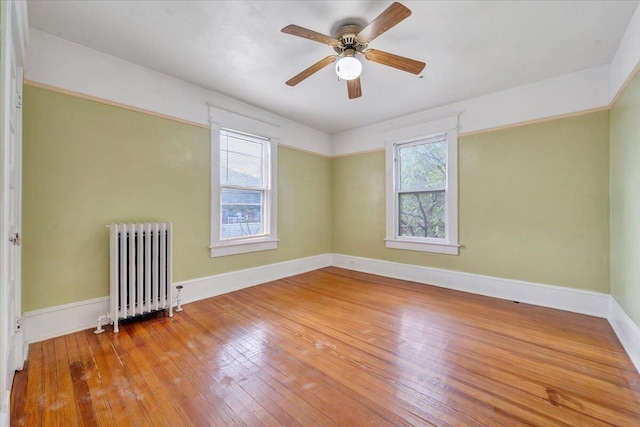 unfurnished room with a wealth of natural light, ceiling fan, radiator heating unit, and hardwood / wood-style flooring