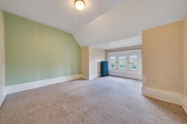 unfurnished living room with vaulted ceiling, light carpet, and radiator heating unit