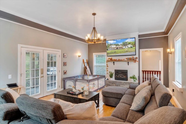 living room featuring hardwood / wood-style floors, a large fireplace, crown molding, an inviting chandelier, and french doors