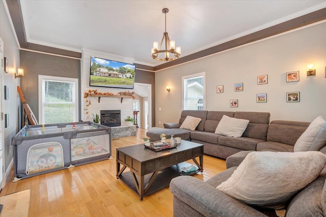 living room with crown molding, a fireplace, light hardwood / wood-style floors, and a notable chandelier