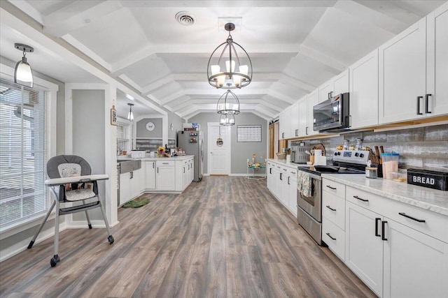 kitchen with vaulted ceiling, pendant lighting, white cabinets, backsplash, and stainless steel appliances