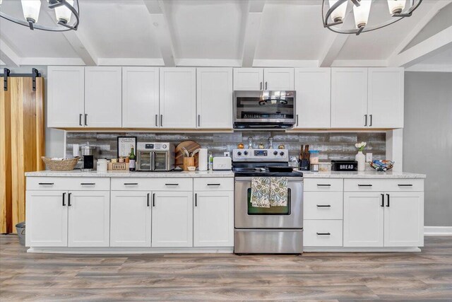 kitchen featuring appliances with stainless steel finishes, a barn door, decorative backsplash, and white cabinets