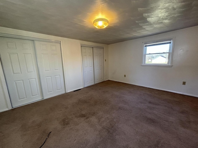 unfurnished bedroom with a textured ceiling, two closets, and dark carpet