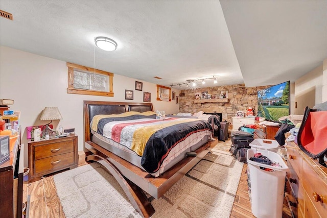 bedroom featuring a fireplace, track lighting, a textured ceiling, and light hardwood / wood-style flooring