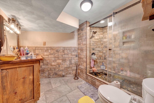 bathroom featuring a textured ceiling, a tile shower, vanity, toilet, and tile walls