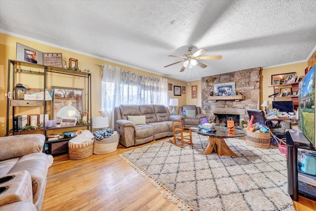 living room with hardwood / wood-style floors, a stone fireplace, a textured ceiling, and ornamental molding