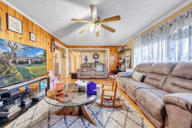 living room with ornamental molding, ceiling fan, a textured ceiling, wood-type flooring, and wooden walls