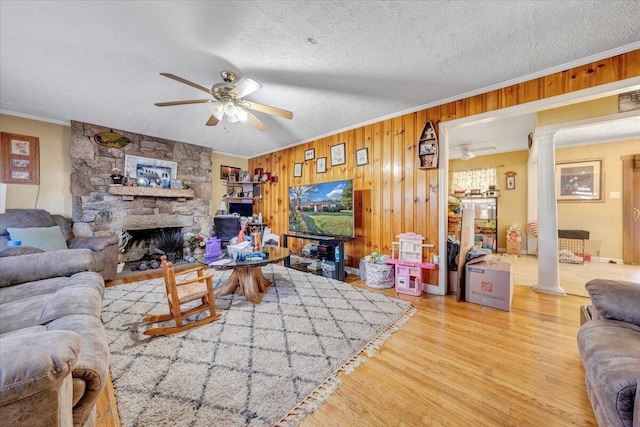 living room with crown molding, a textured ceiling, wood walls, hardwood / wood-style flooring, and decorative columns