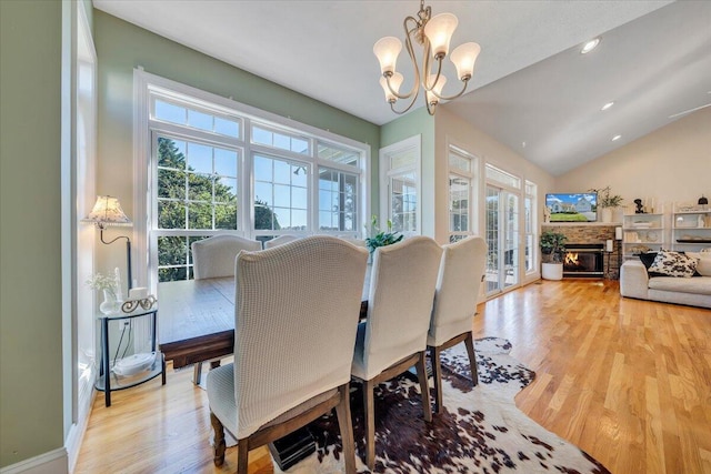 dining space featuring light hardwood / wood-style flooring, a fireplace, vaulted ceiling, and a chandelier