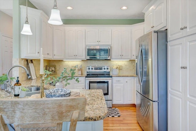 kitchen with stainless steel appliances, hanging light fixtures, sink, and white cabinetry