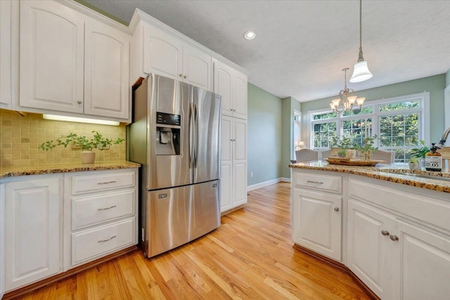 kitchen featuring light wood-type flooring, decorative backsplash, white cabinets, pendant lighting, and stainless steel refrigerator with ice dispenser