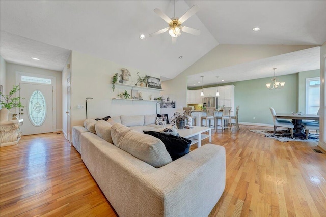 living room with lofted ceiling, ceiling fan with notable chandelier, and light hardwood / wood-style flooring