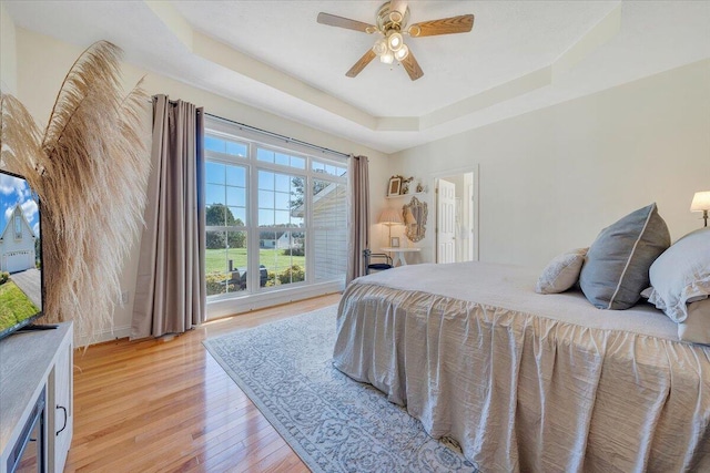 bedroom featuring a raised ceiling, light wood-type flooring, and ceiling fan