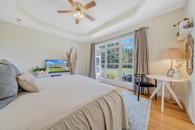 bedroom with light hardwood / wood-style floors, a tray ceiling, and ceiling fan