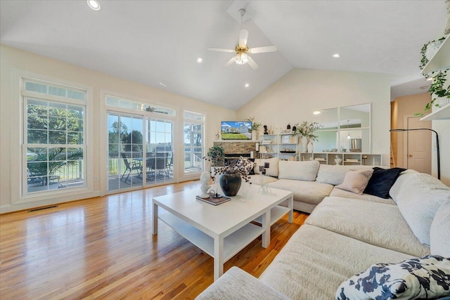 living room with ceiling fan, a stone fireplace, light hardwood / wood-style floors, and high vaulted ceiling