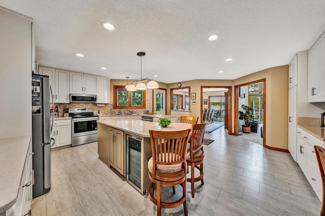 kitchen featuring a center island, white cabinetry, stainless steel appliances, pendant lighting, and wine cooler