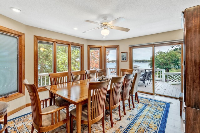 tiled dining space featuring a water view, ceiling fan, and a textured ceiling