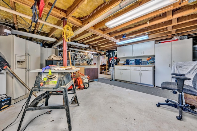 basement featuring white refrigerator with ice dispenser and a workshop area