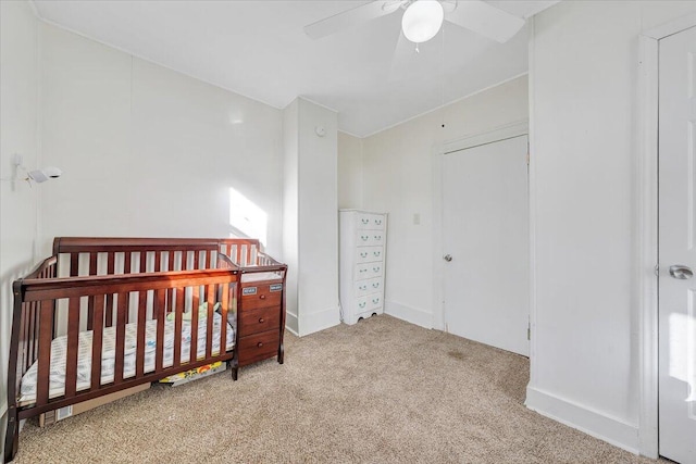 bedroom featuring a nursery area, light colored carpet, and ceiling fan