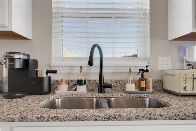 room details with white cabinetry, sink, and light stone counters