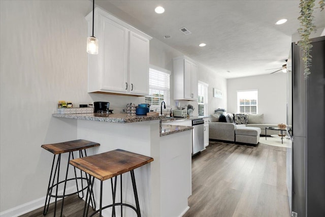 kitchen with stainless steel appliances, dark wood-type flooring, a kitchen breakfast bar, white cabinetry, and dark stone countertops