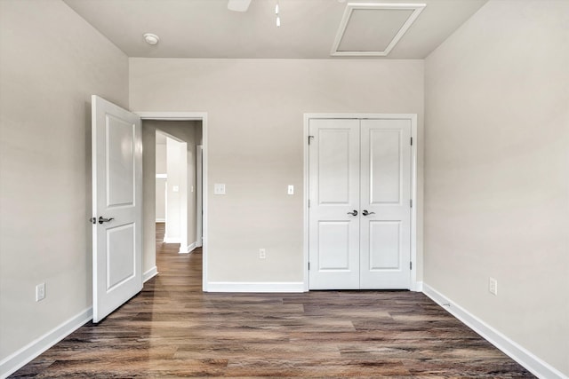 unfurnished bedroom with dark wood-style floors, attic access, and baseboards