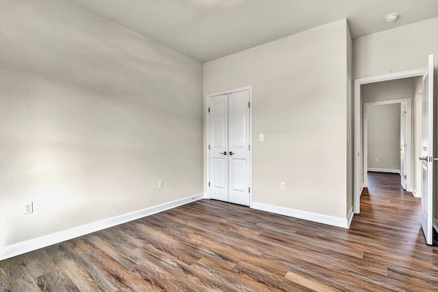 unfurnished bedroom featuring a closet, dark wood-style flooring, and baseboards