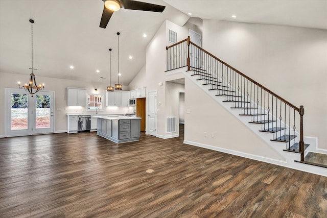 unfurnished living room with stairs, dark wood finished floors, visible vents, baseboards, and ceiling fan with notable chandelier