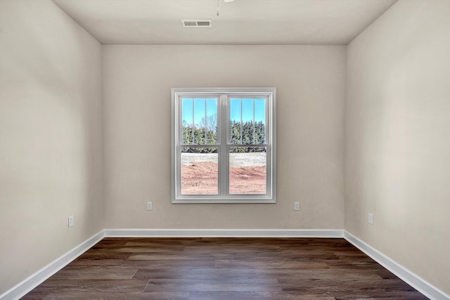 spare room with dark wood-type flooring, visible vents, and baseboards