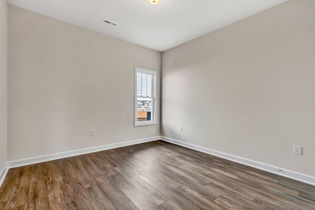 spare room with dark wood-style flooring, visible vents, and baseboards