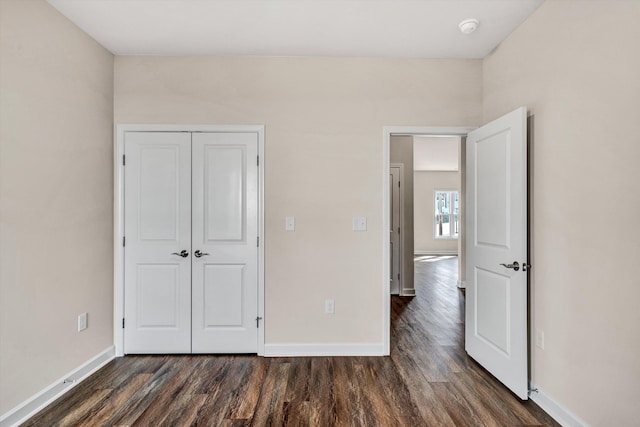 unfurnished bedroom with dark wood-type flooring, a closet, and baseboards