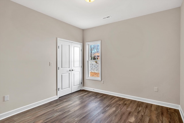 spare room with dark wood-style flooring, visible vents, and baseboards