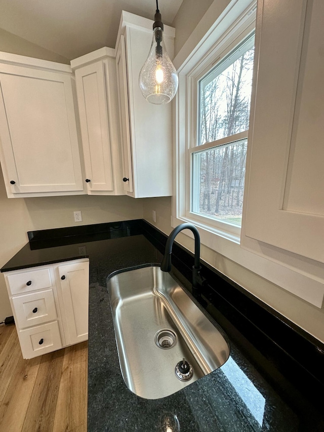 kitchen featuring sink, white cabinetry, hanging light fixtures, dark stone countertops, and light hardwood / wood-style floors