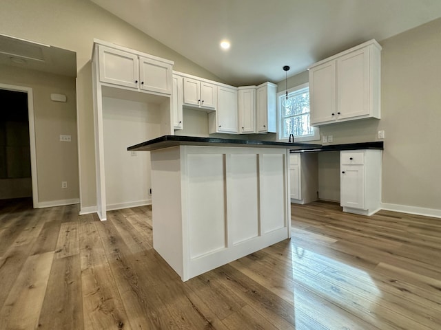 kitchen with white cabinetry, vaulted ceiling, hanging light fixtures, light hardwood / wood-style flooring, and a kitchen island