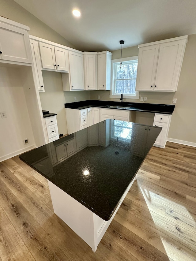 kitchen featuring lofted ceiling, sink, light hardwood / wood-style flooring, white cabinets, and decorative light fixtures