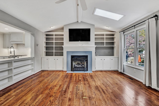 unfurnished living room featuring sink, lofted ceiling with beams, a tile fireplace, ceiling fan, and light hardwood / wood-style flooring