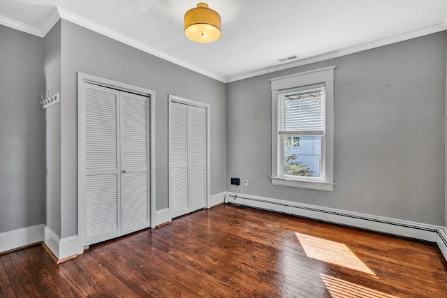 unfurnished bedroom featuring dark wood-type flooring, a baseboard heating unit, two closets, and crown molding