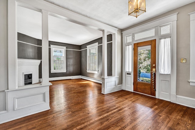 foyer entrance with a baseboard radiator, dark wood-type flooring, a notable chandelier, and a fireplace