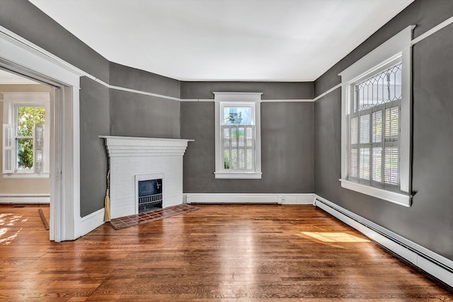 unfurnished living room featuring baseboard heating, wood-type flooring, and a brick fireplace