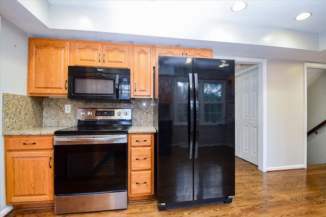 kitchen featuring black appliances, light stone countertops, dark hardwood / wood-style floors, and backsplash