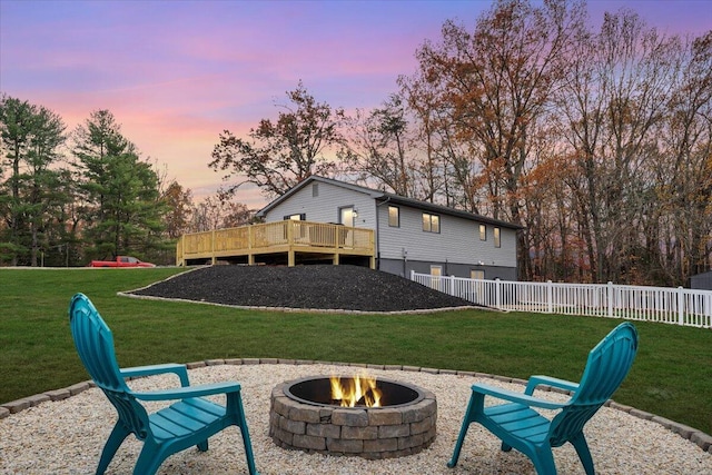 back house at dusk with an outdoor fire pit, a lawn, and a wooden deck