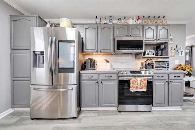 kitchen with gray cabinetry, decorative backsplash, stainless steel appliances, and ornamental molding