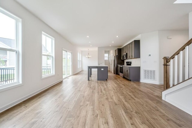 kitchen with a notable chandelier, light wood-type flooring, stainless steel appliances, and an island with sink