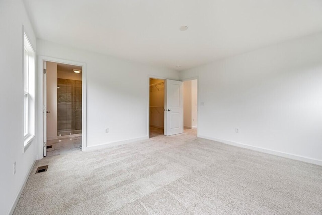 unfurnished bedroom featuring light carpet, a walk in closet, a closet, and connected bathroom