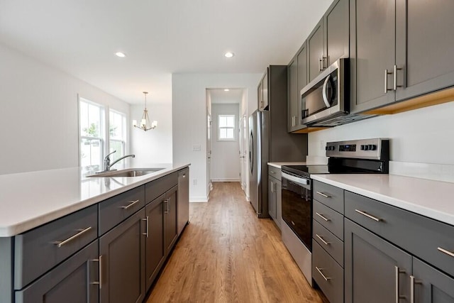 kitchen featuring sink, light hardwood / wood-style floors, stainless steel appliances, pendant lighting, and an inviting chandelier