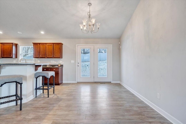 kitchen with sink, decorative light fixtures, an inviting chandelier, a kitchen breakfast bar, and light hardwood / wood-style flooring